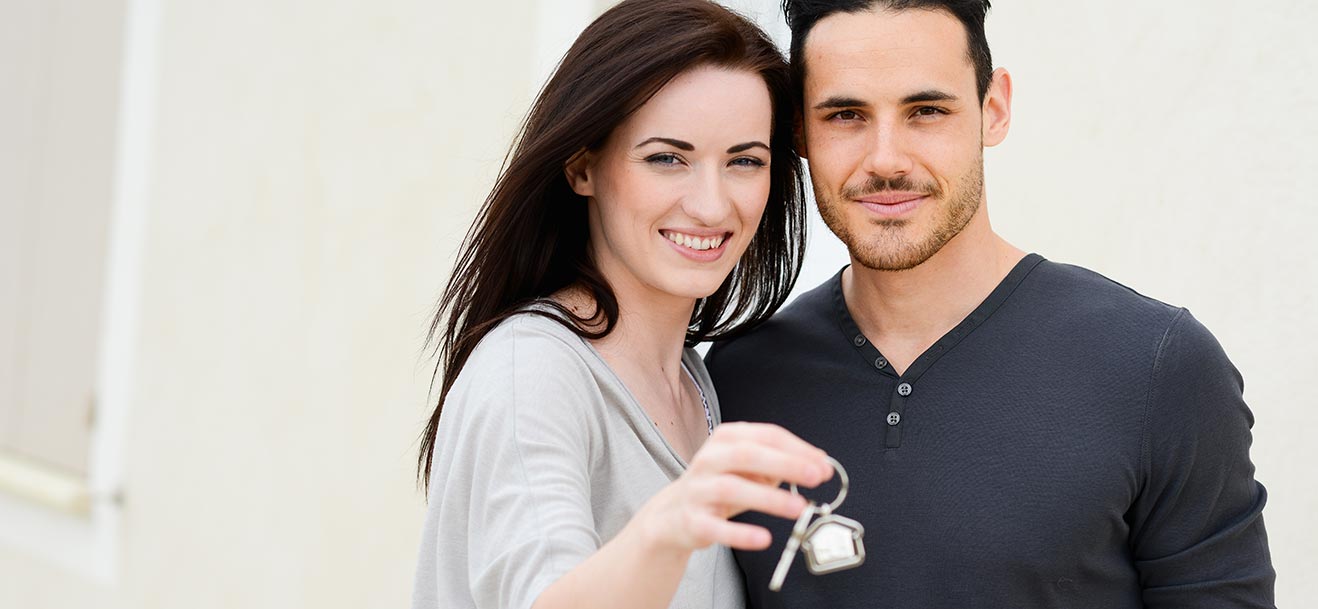 ein junges Paar mit dem Schlüssel des neu erworbenen Hauses in der Hand